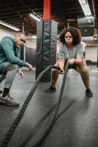 A trainer watches a person performing battle rope exercises in a gym. A trainer watches a person performing battle rope exercises in a gym.