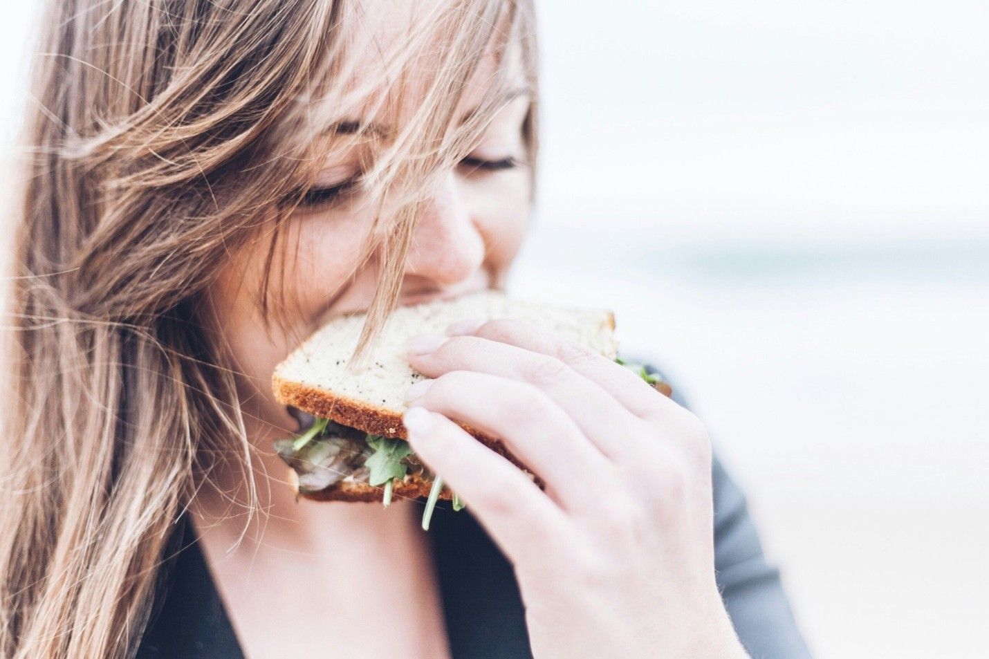 A person with long hair smiles while holding a sandwich near their mouth to take a bite. A person with long hair smiles while holding a sandwich near their mouth to take a bite.