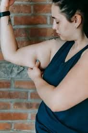 A person wearing a dark tank top pinching the skin on their upper arm against a brick wall background. A person wearing a dark tank top pinching the skin on their upper arm against a brick wall background.