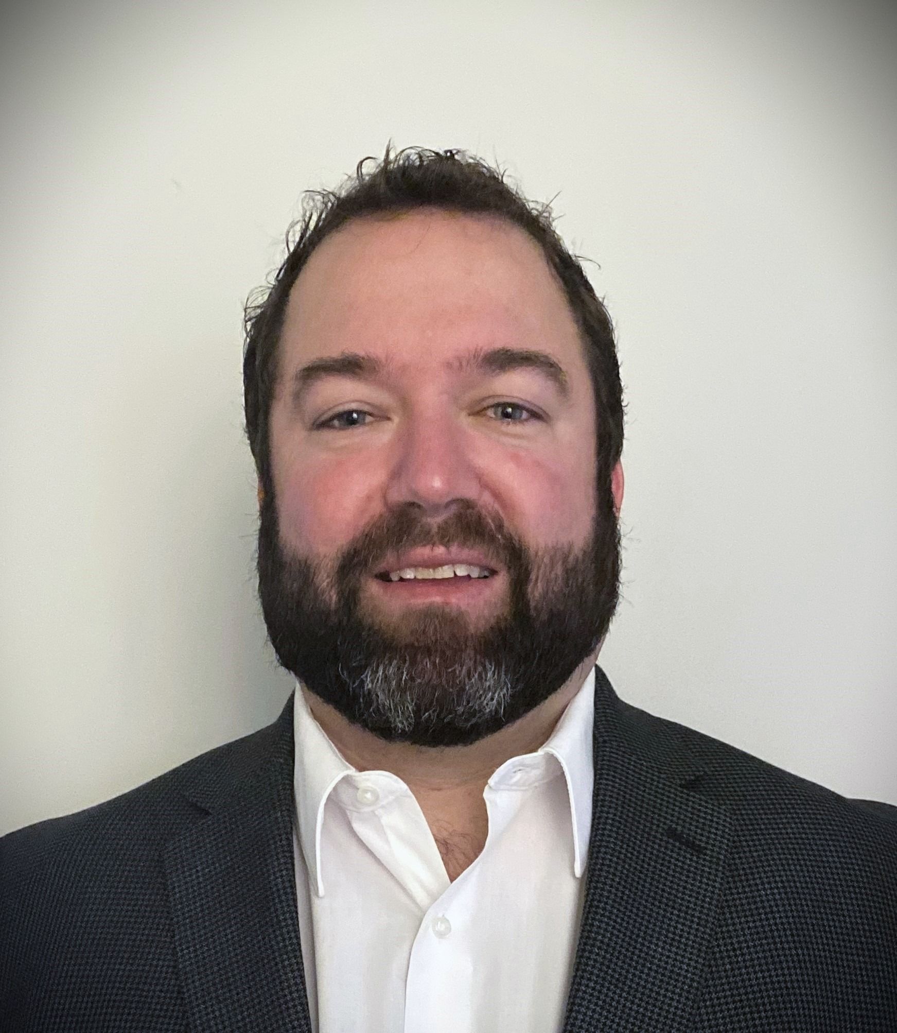 A man with a beard is wearing a suit and white shirt.