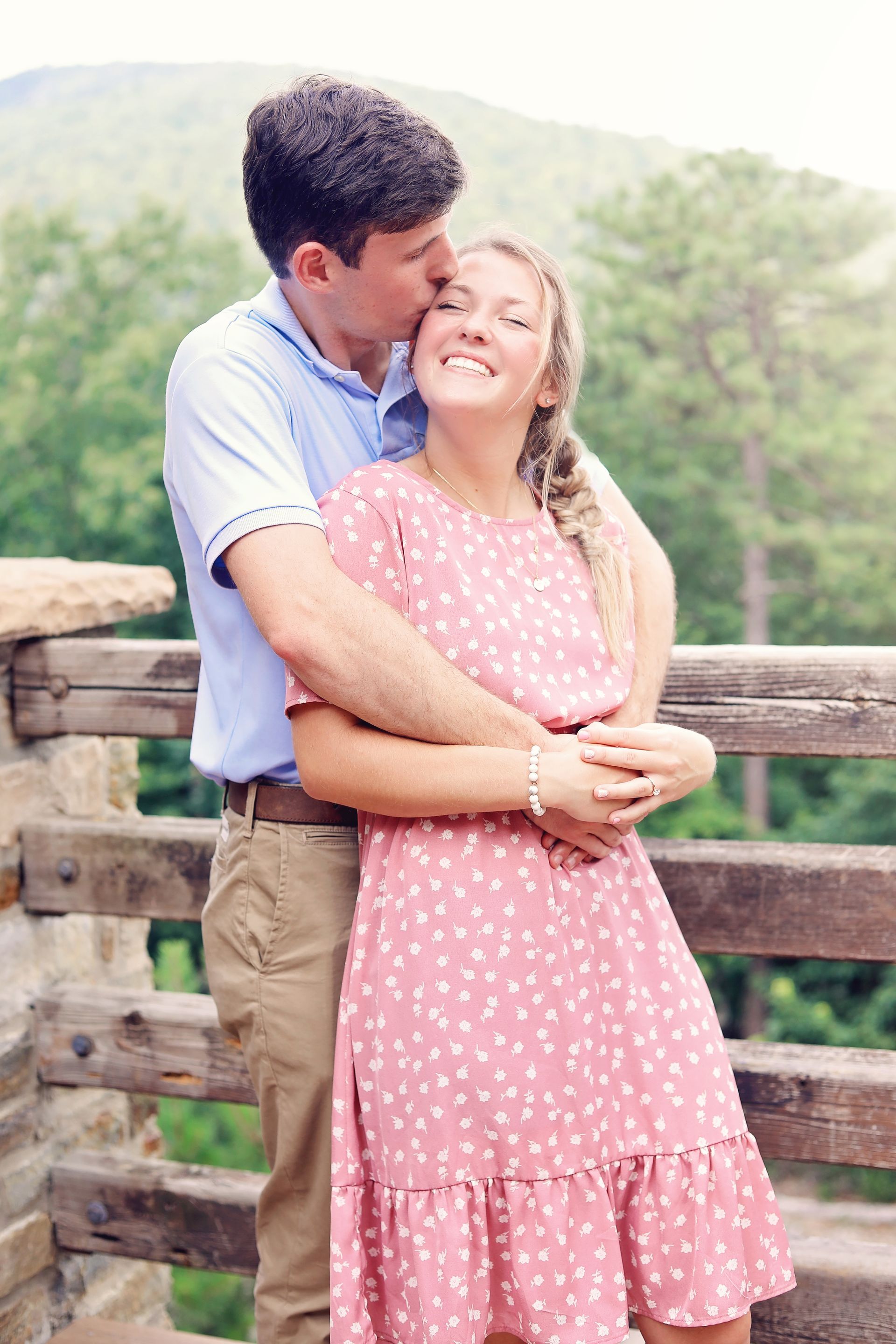 Couple embracing on a wooden bridge, smiling in a soft outdoor setting.