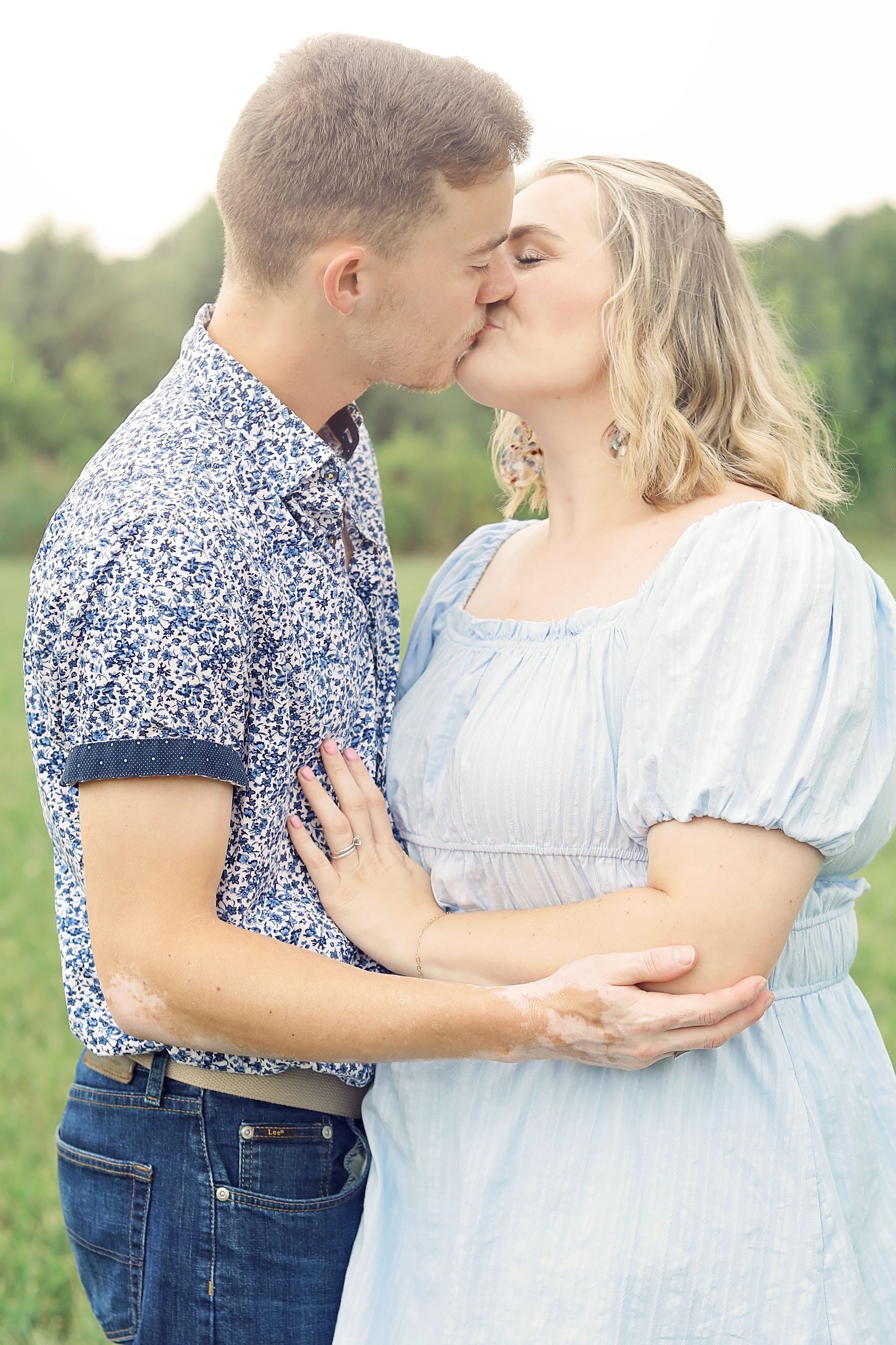 Couple kissing outdoors, holding each other with blurred green background.