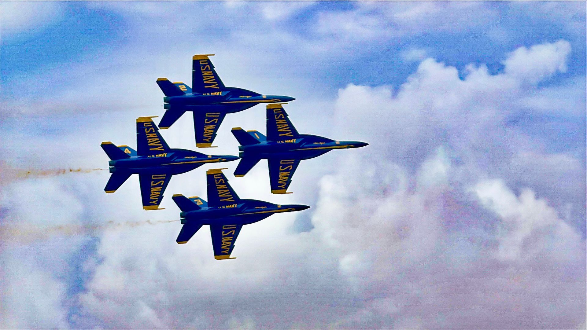 Four blue and yellow fighter jets flying in tight formation against a cloudy sky