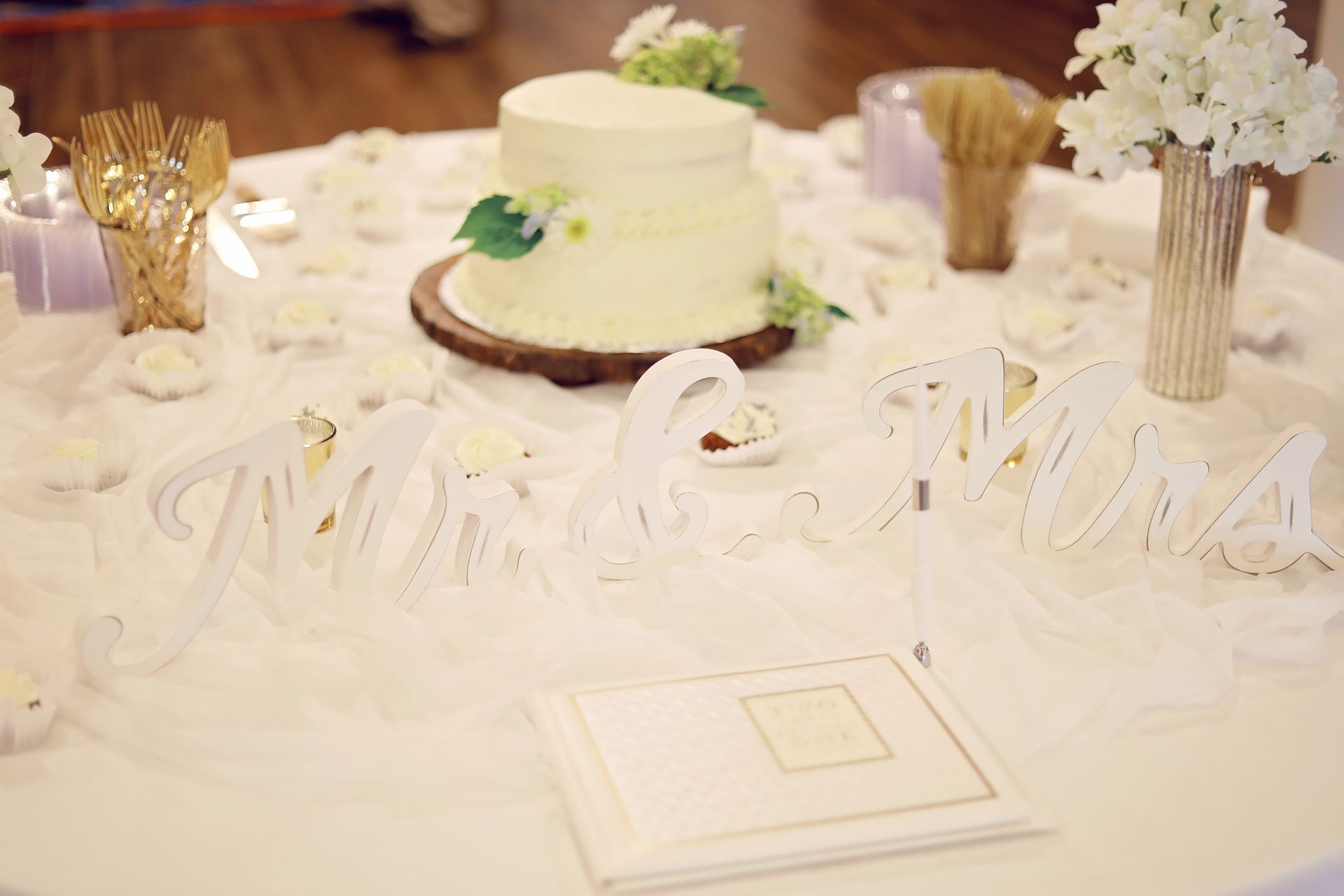 White-decorated wedding reception table with a cake, flowers, and decorative place cards