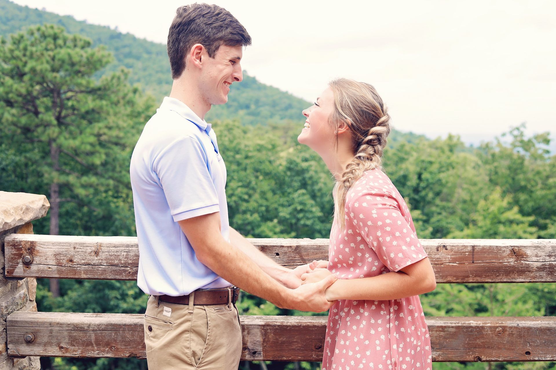 Couple holding hands and smiling on a wooden overlook with green hills in the background