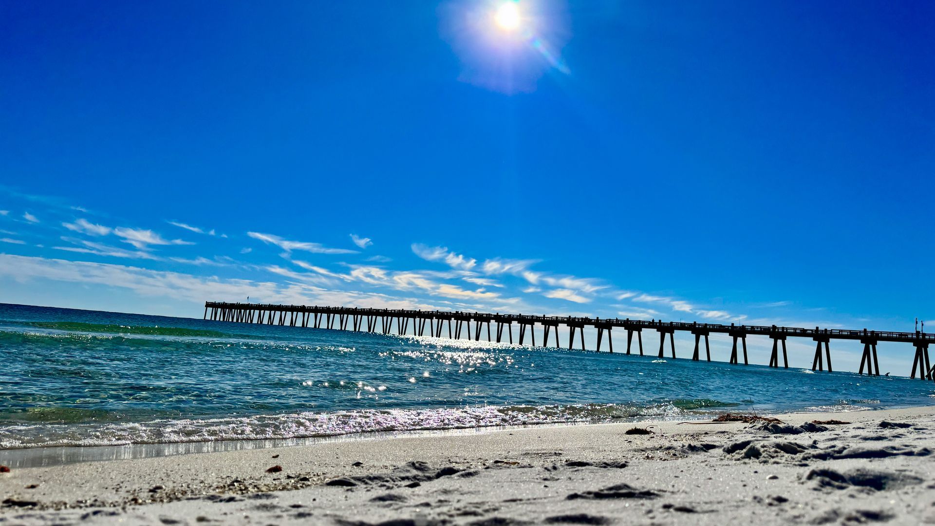 Sandy beach with turquoise water and a long pier under a bright blue sky.