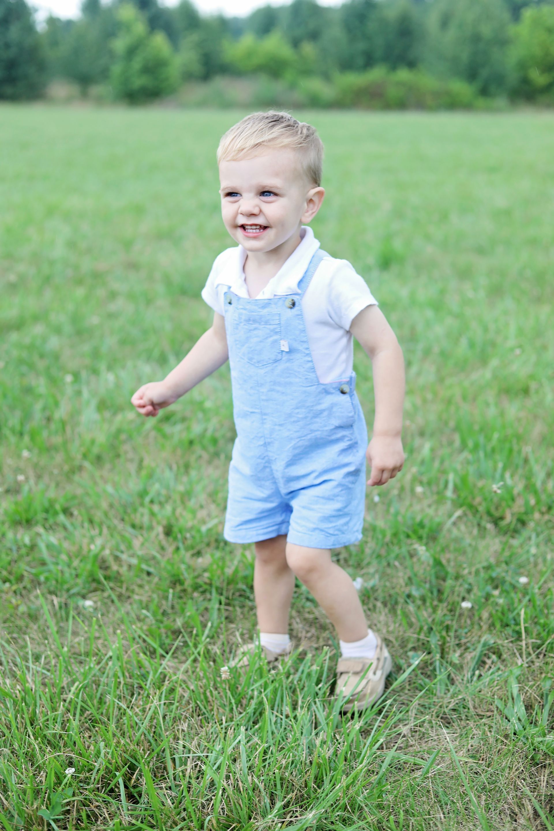 Smiling child in blue overalls standing in a grassy field