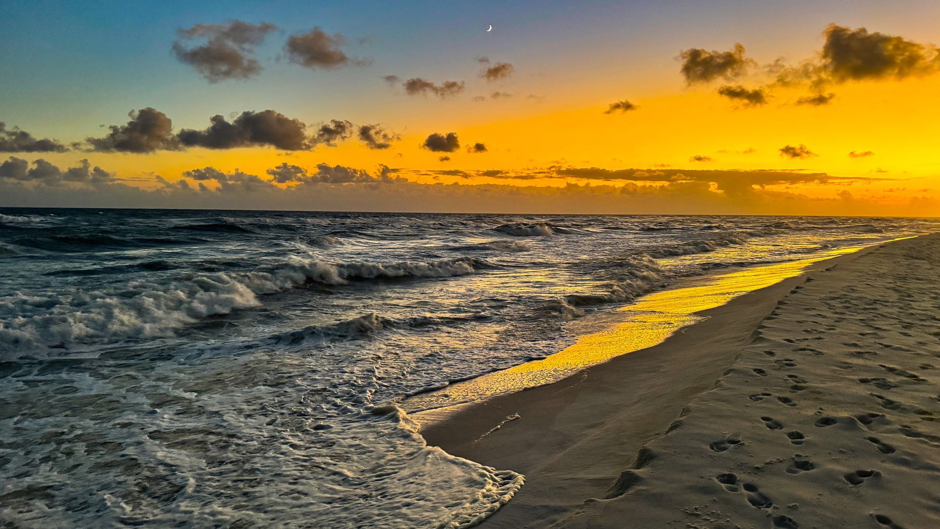 Golden sunset over a sandy beach with waves rolling in and scattered clouds overhead