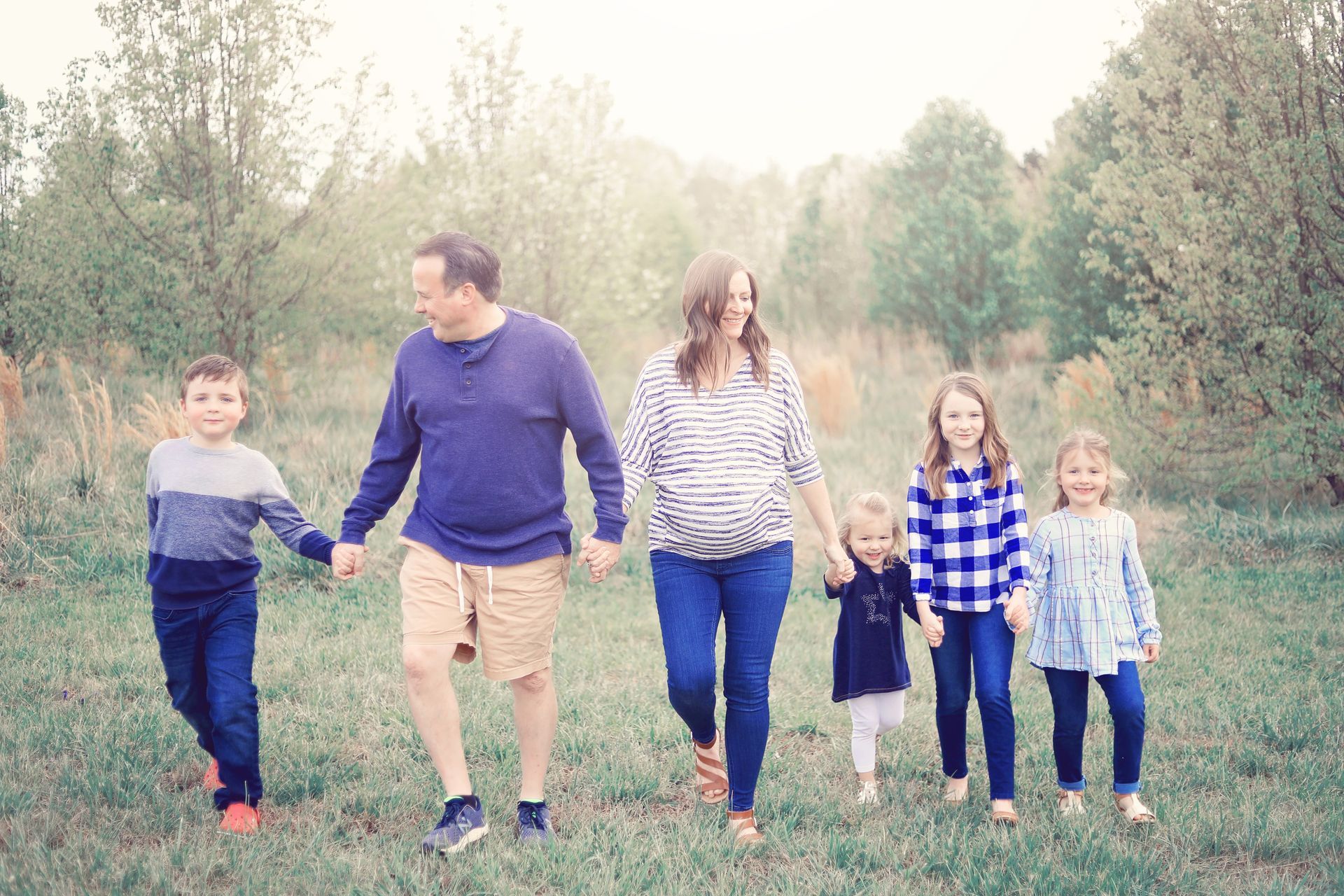 Family walking hand in hand through a grassy field with trees in the background