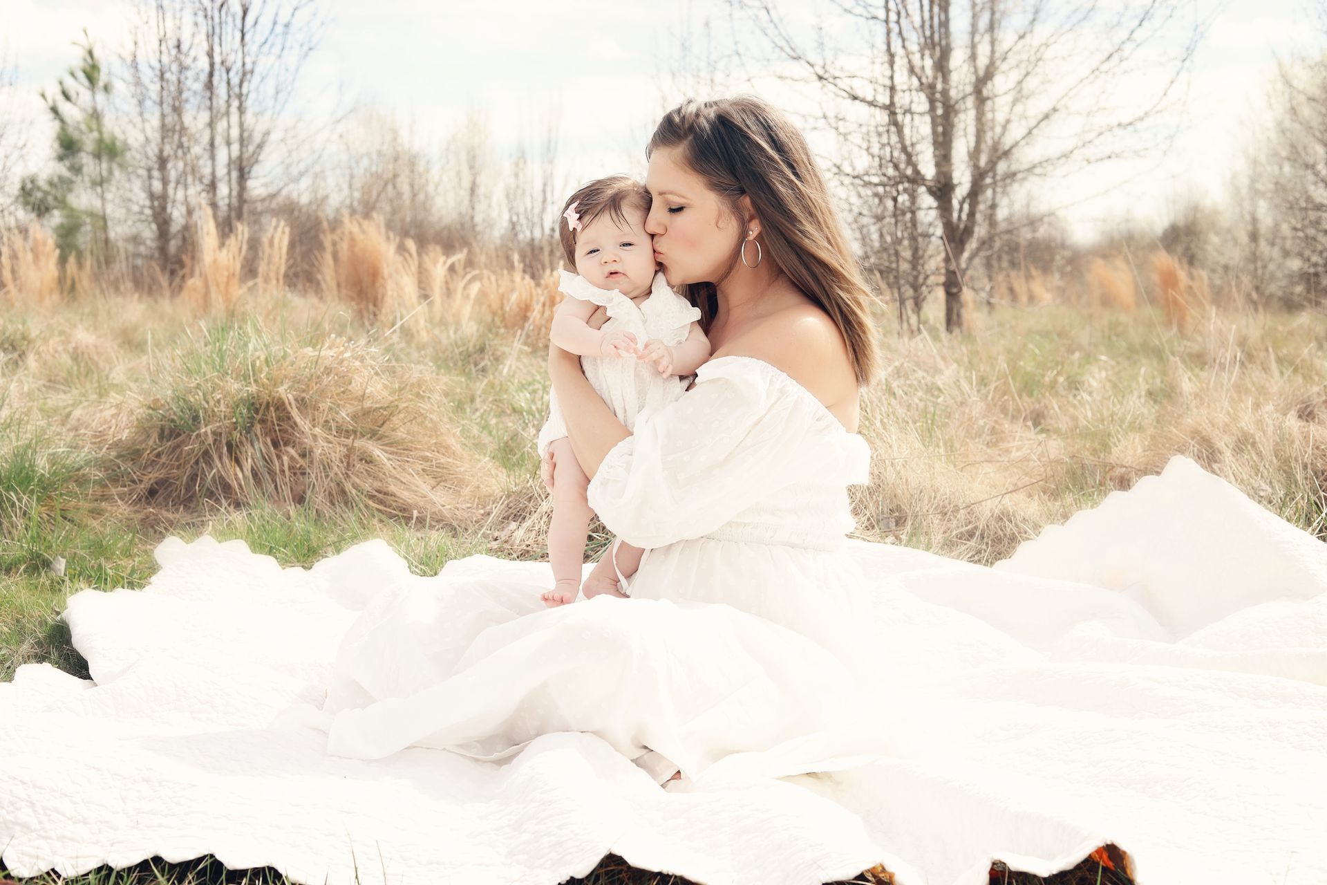 Mother holding a baby in a white dress outdoors in a sunlit field