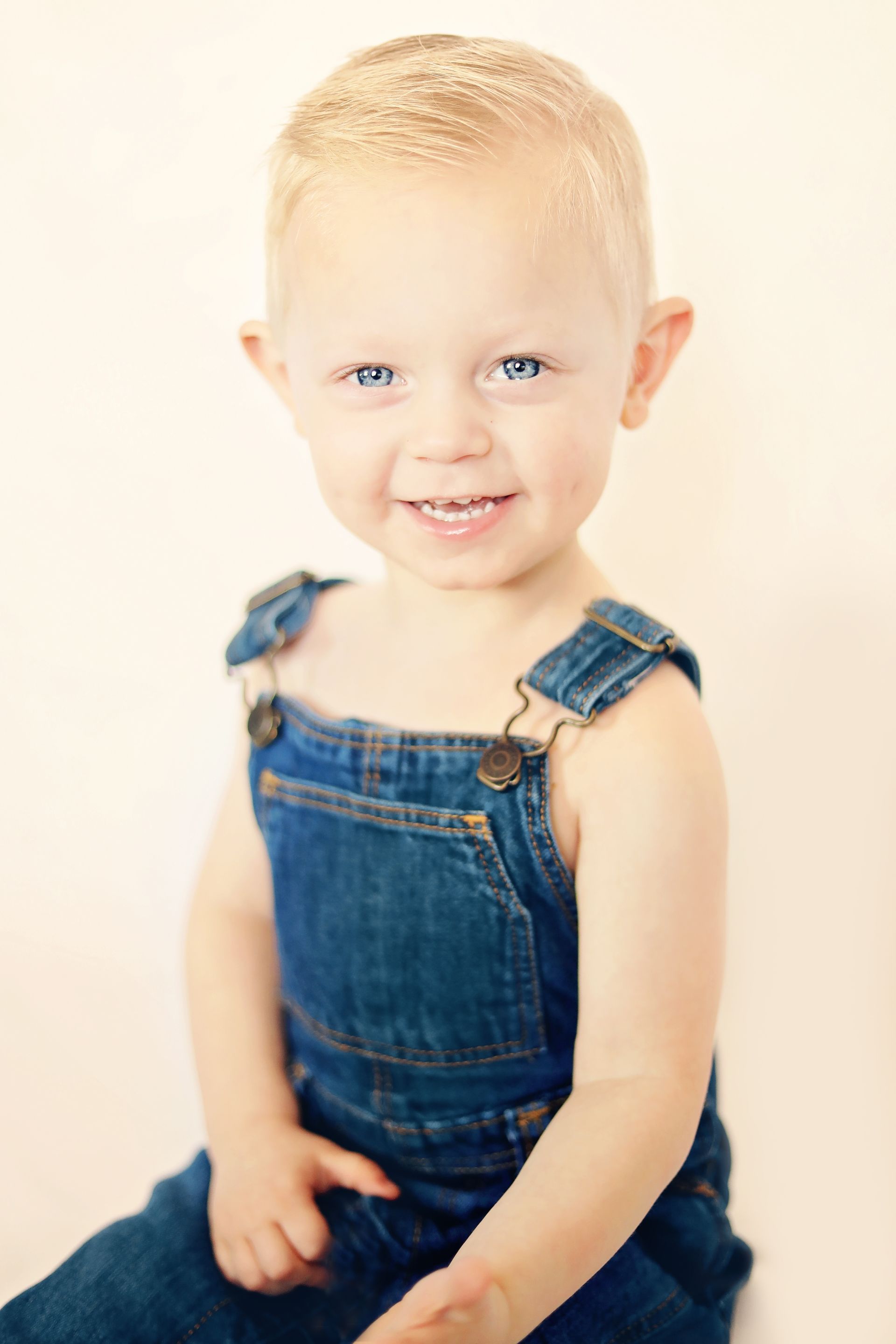 Smiling child in blue denim overalls sitting against a light background