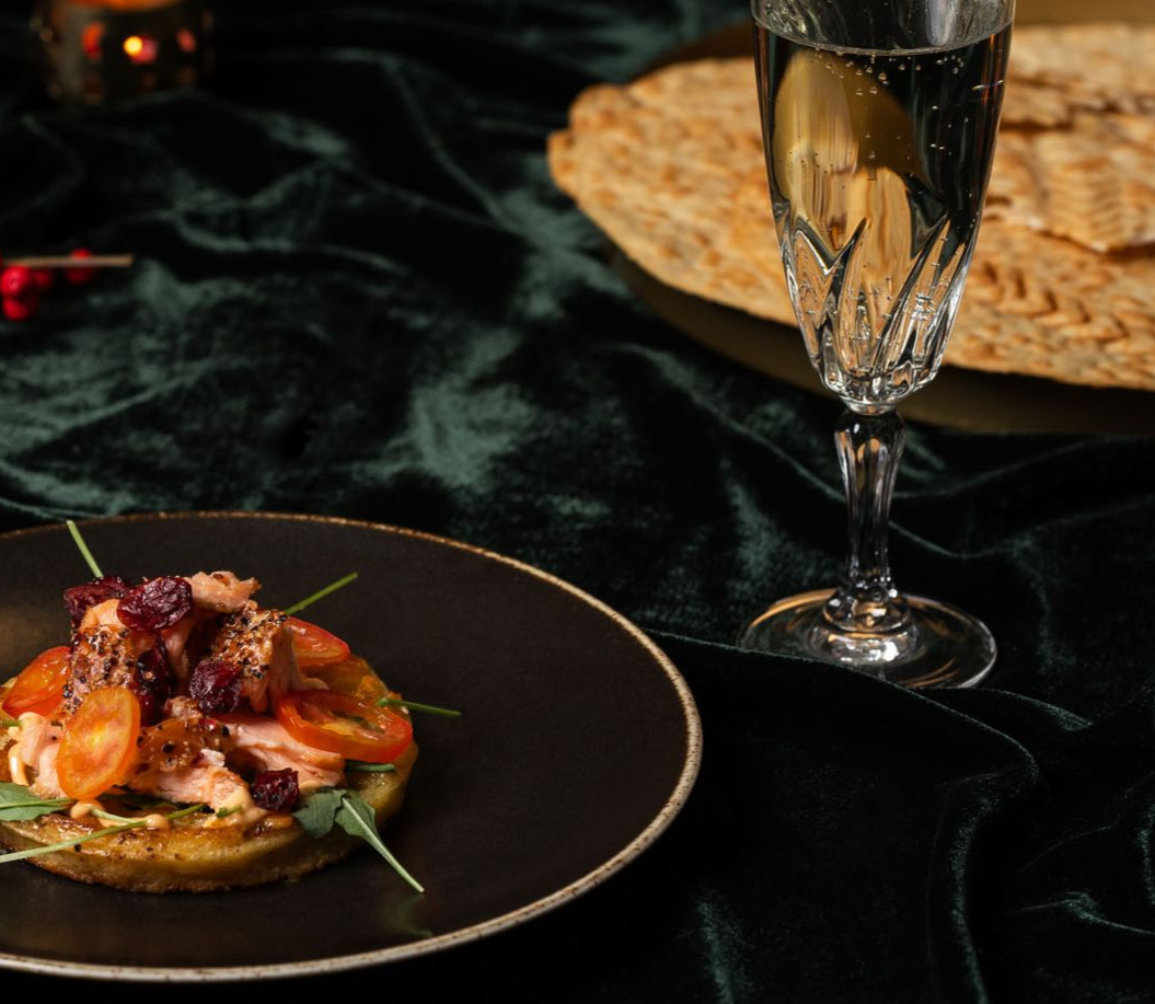 Forréttur á dökkum diski með kampavínsglasi og matzah á grænum dúk.