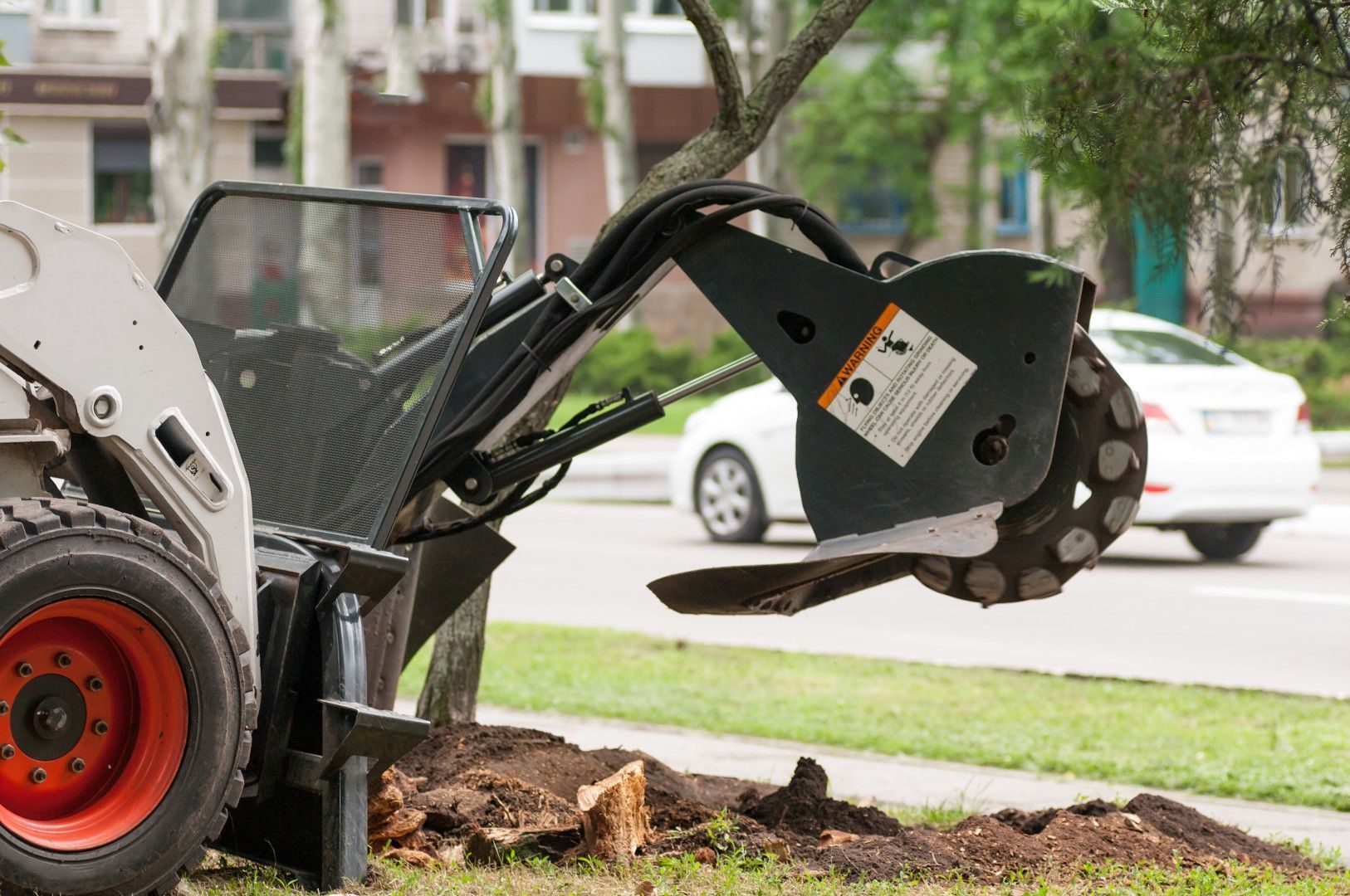 A bobcat is stump grinding a tree stump on the side of the road.