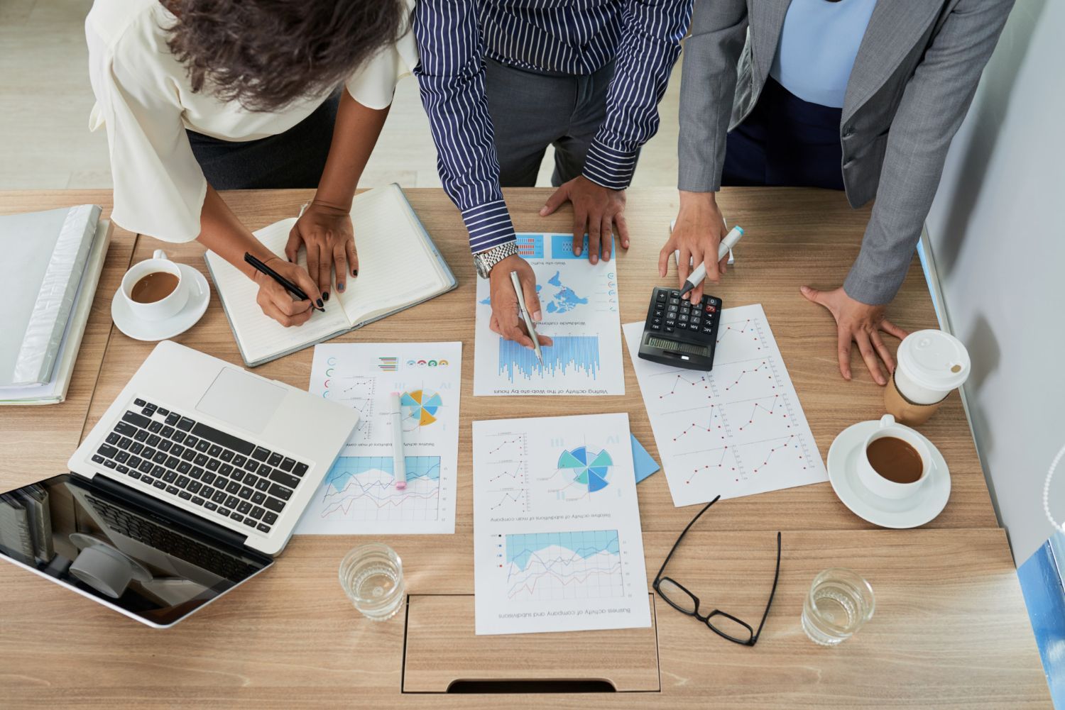 Tres personas revisan informes financieros alrededor de una mesa, utilizando una computadora portátil