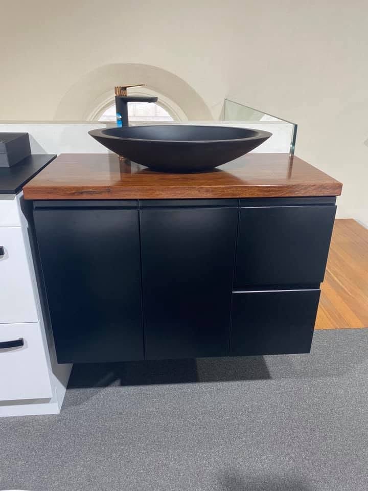 Modern bathroom vanity with black sink, wood countertop, and dark cabinets against a tiled wall