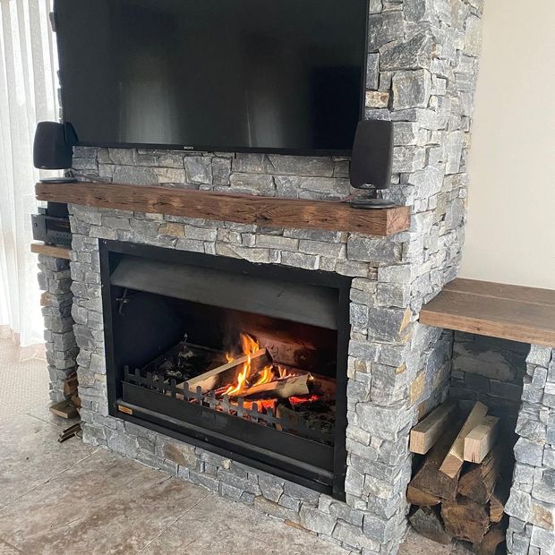 Stone fireplace with a lit fire, a TV above, and stacked firewood on the right Stone fireplace with a lit fire, a TV above, and stacked firewood on the right