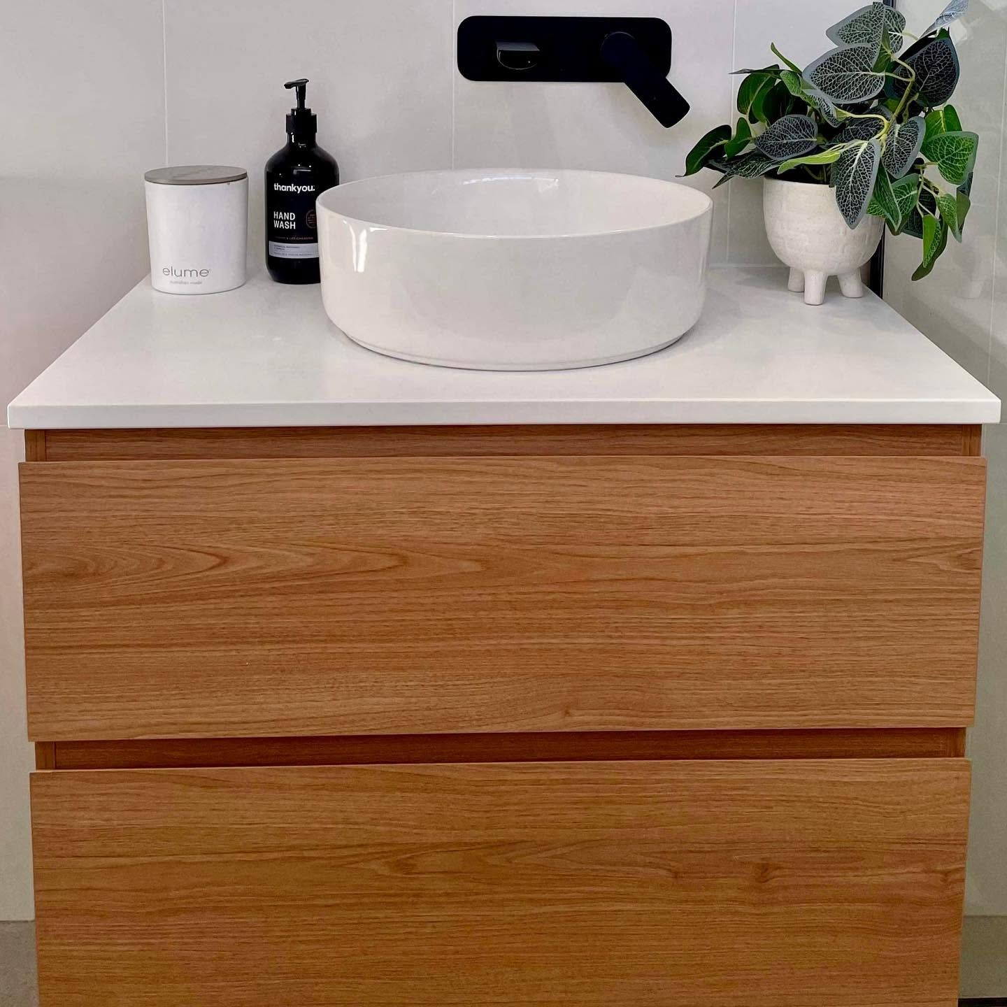 Modern bathroom vanity with white countertop, round sink, black faucet, and small plant décor