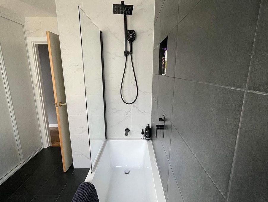 Modern bathroom with white bathtub, dark gray tiled wall, shower fixtures, and a wall-mounted mirror cabinet Modern bathroom with white bathtub, dark gray tiled wall, shower fixtures, and a wall-mounted mirror cabinet