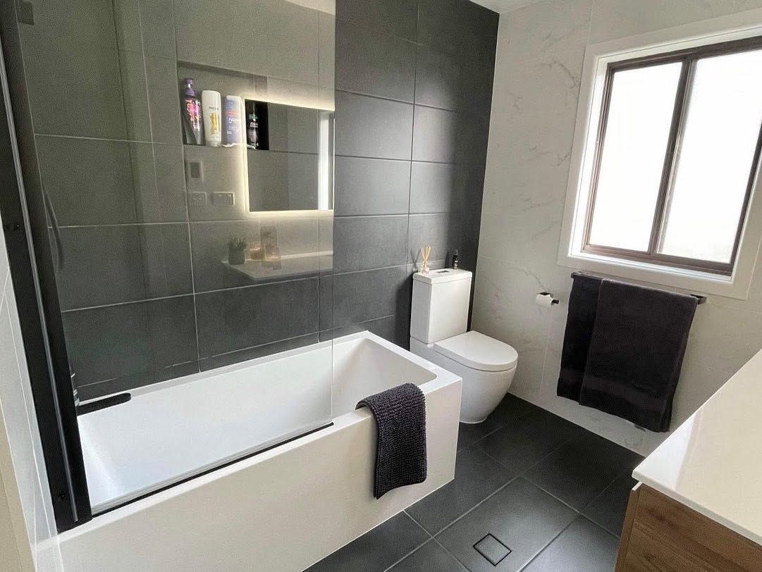 Modern bathroom with bathtub, toilet, dark tile walls, and a window with a towel rail