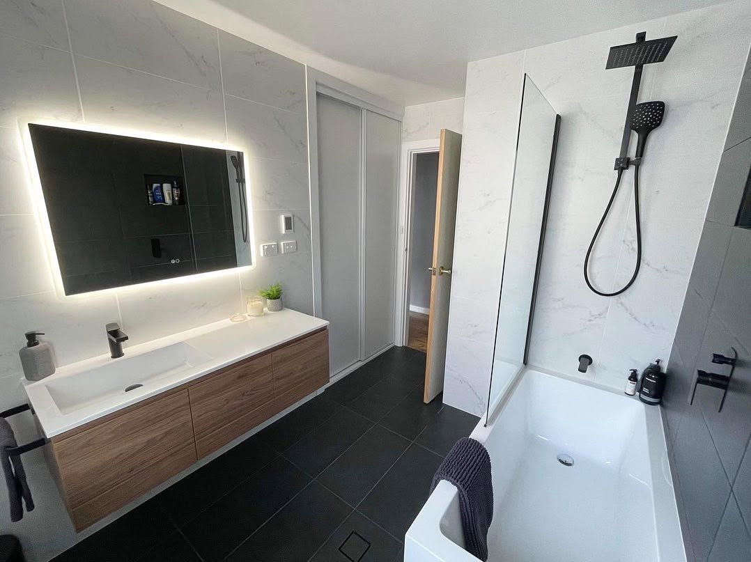 Modern bathroom with lit mirror, wood vanity, walk-in shower, and black fixtures