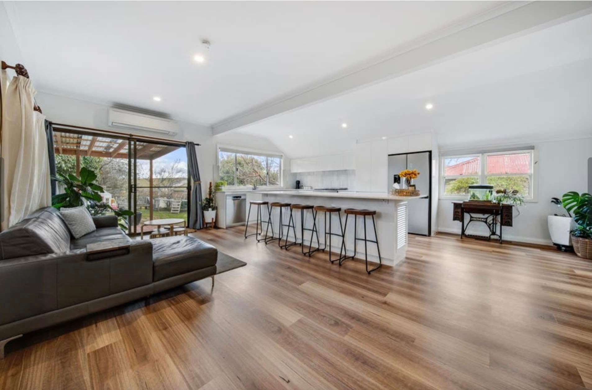 Bright modern living room with gray sofa, long kitchen island, wood floors, and large windows.