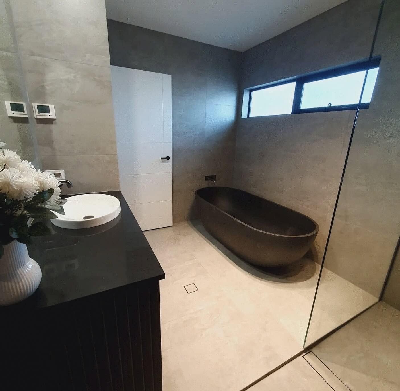 Modern bathroom with black vanity, white sink, freestanding tub, and glass shower wall