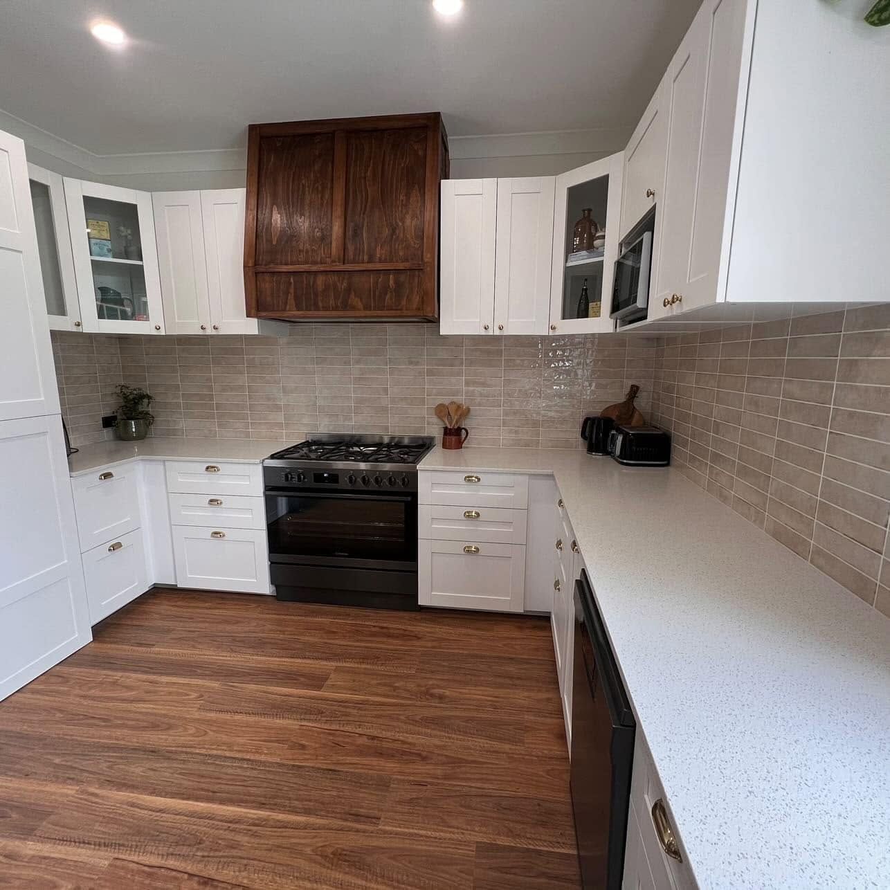 Bright white kitchen with wood floor, black stove, beige tile backsplash, and wood range hood