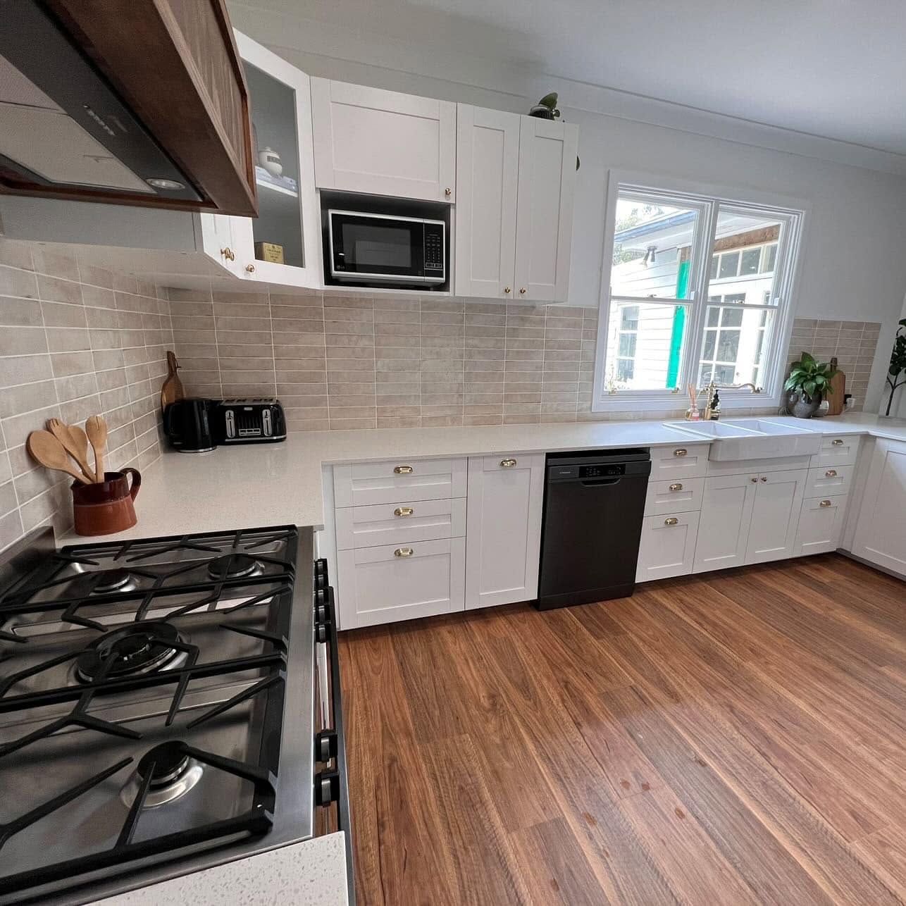 Bright modern kitchen with white cabinets, stainless appliances, beige backsplash, and wood floor