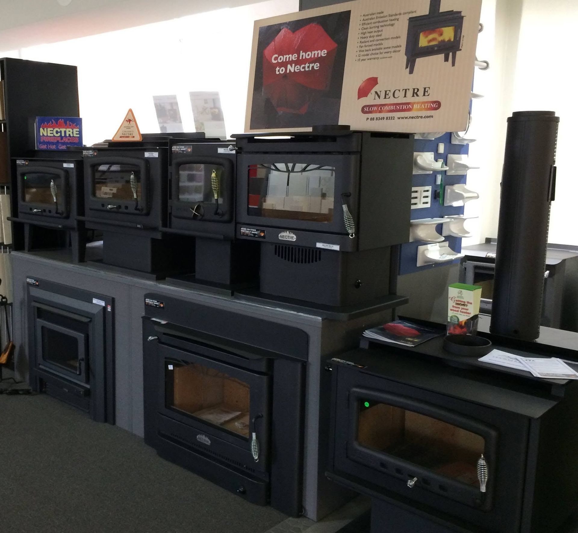 Display of black wood stoves in a showroom with signs and brochures above them