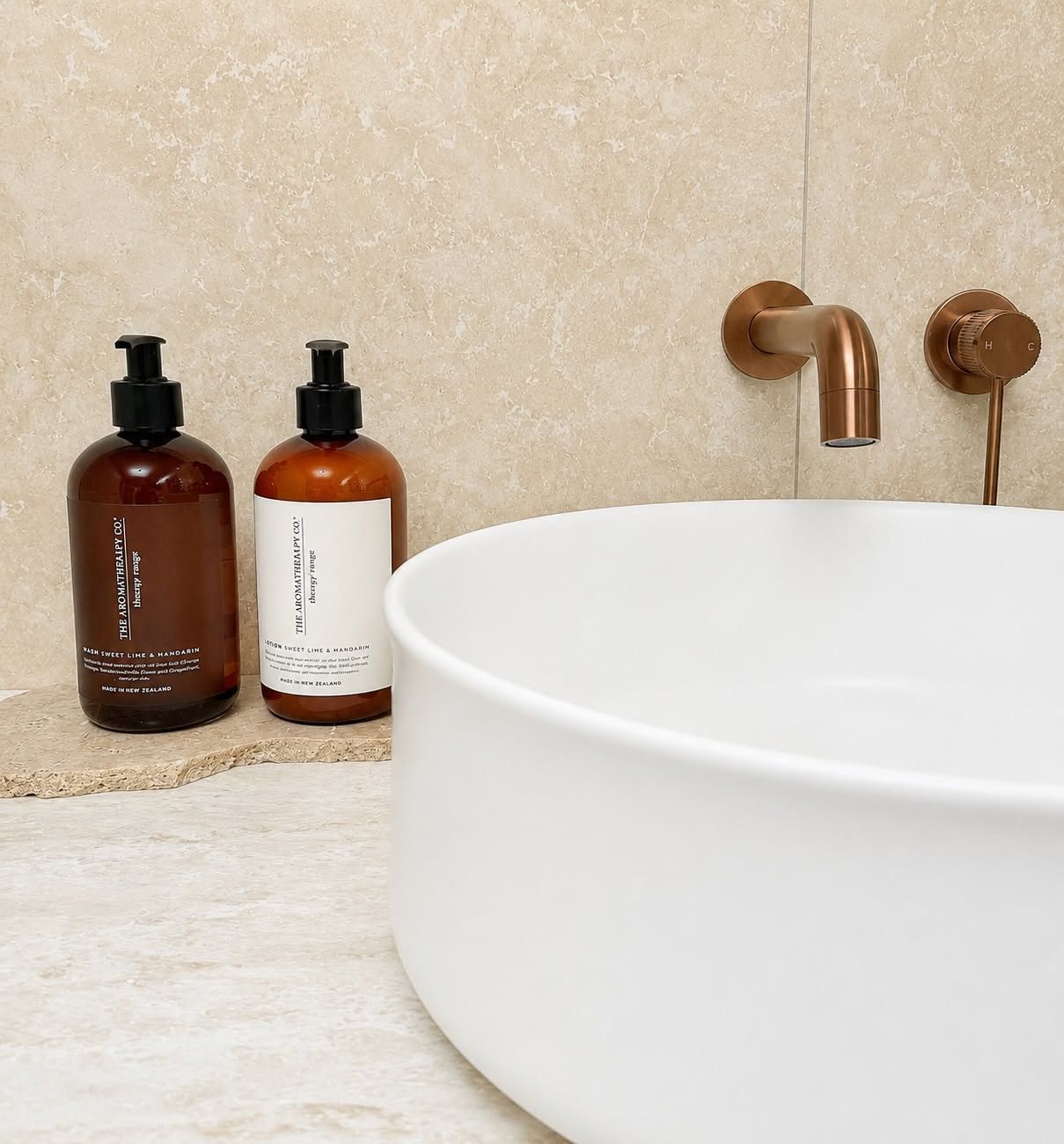 Modern bathroom sink with white basin, brass faucets, and amber soap dispensers on a beige countertop