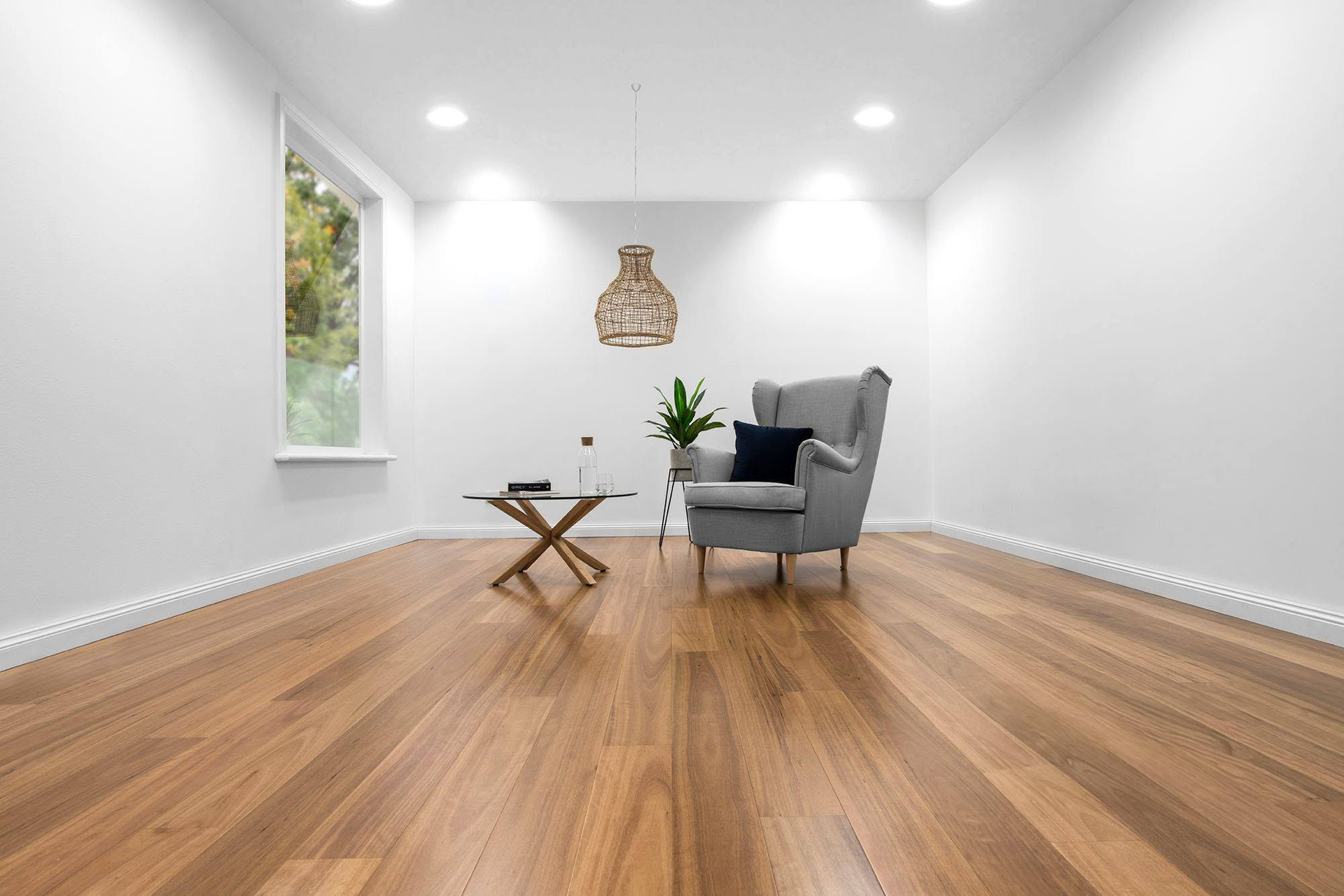 Bright empty living room with hardwood floors, gray armchair, small table, plant, and wall art.