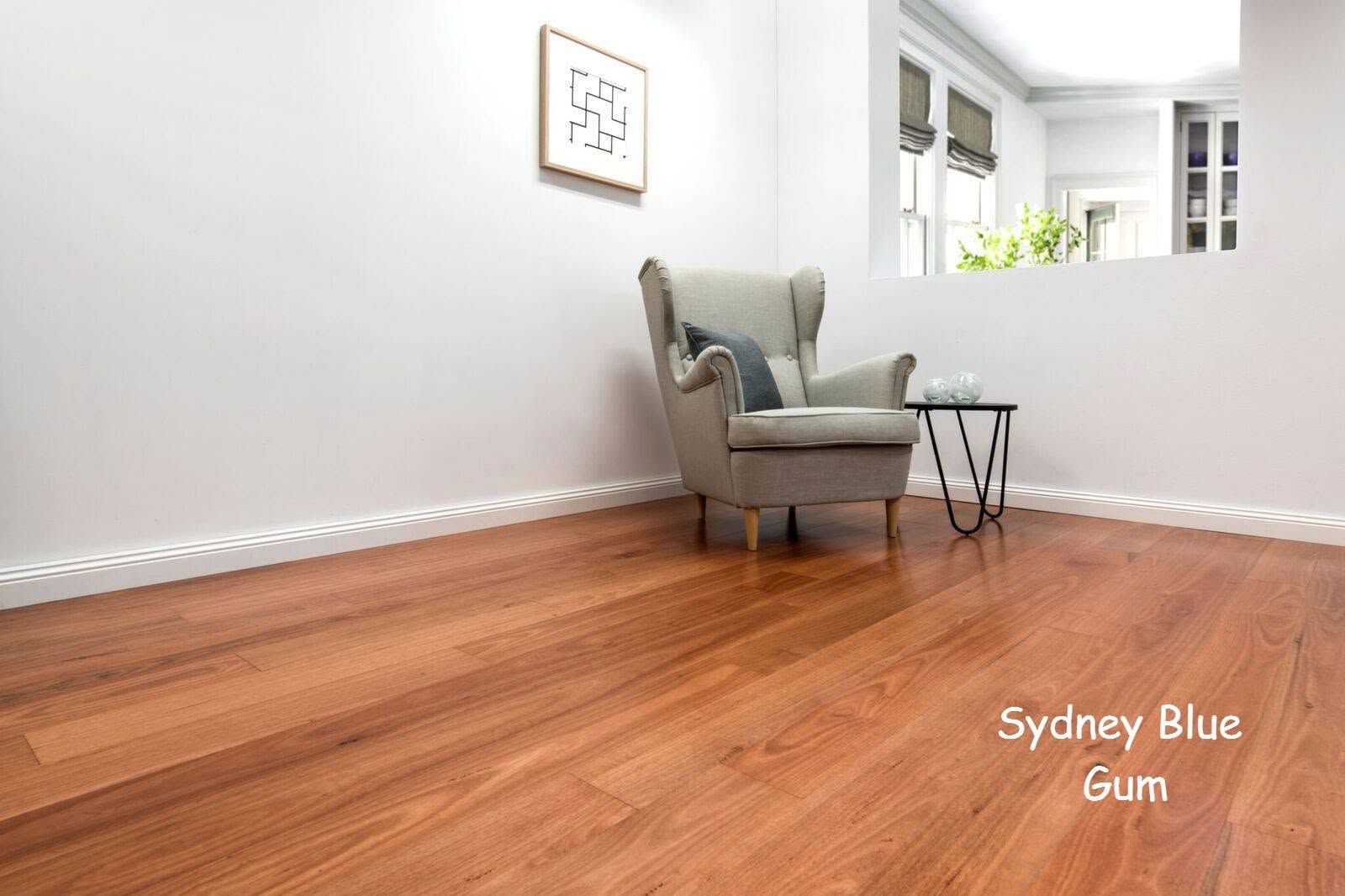 Empty room with honey-toned wood floor, gray armchair, and small side table by a bright window.