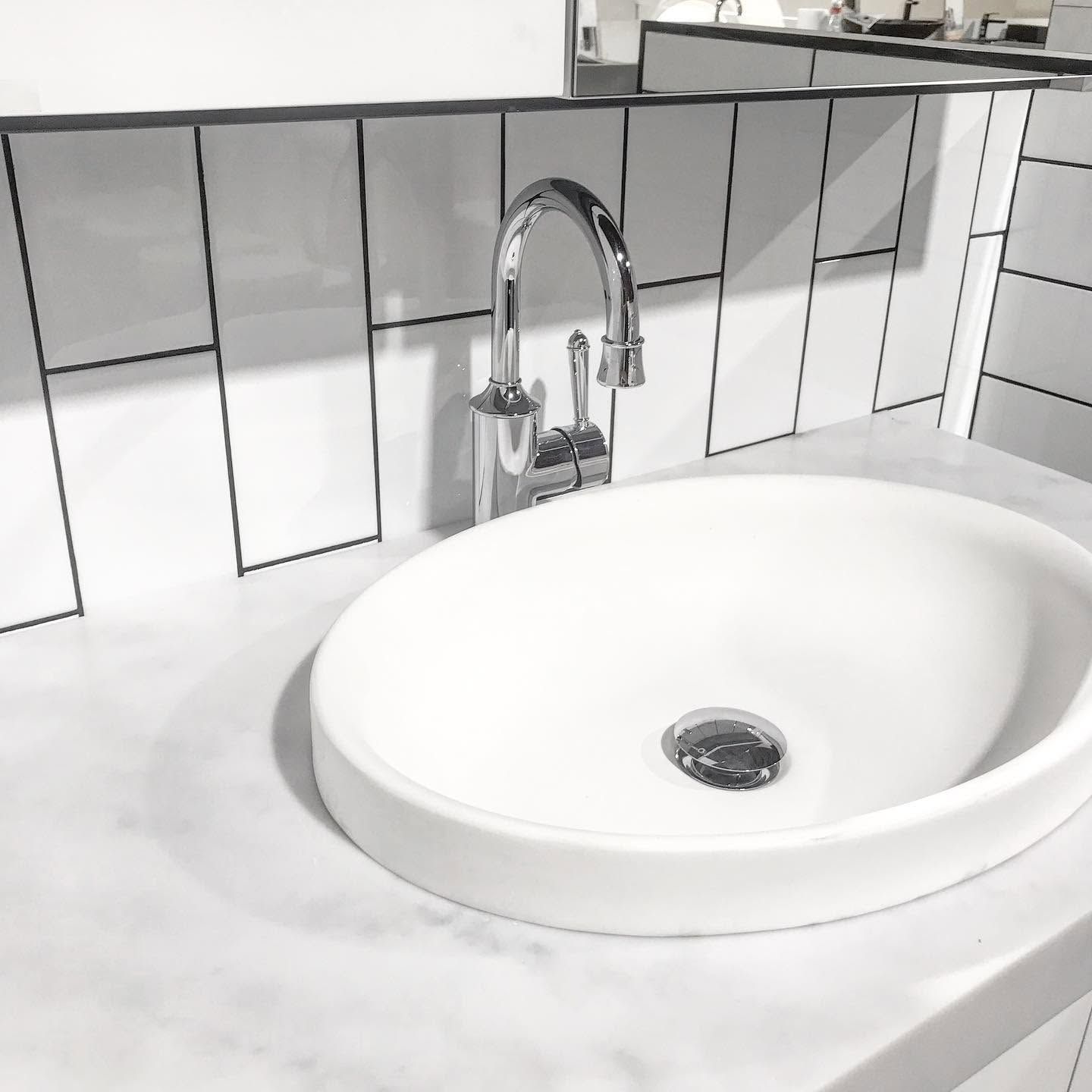 White bathroom sink with chrome faucet on a marble countertop and tiled backsplash