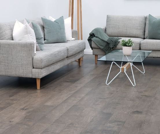 Modern living room with gray sofas, teal cushions, glass coffee table, and dark wood flooring