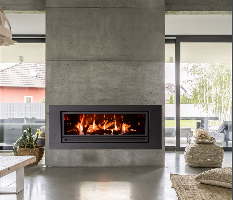Modern living room with concrete fireplace and glass doors, lit fire, stone decor, and woven rug.