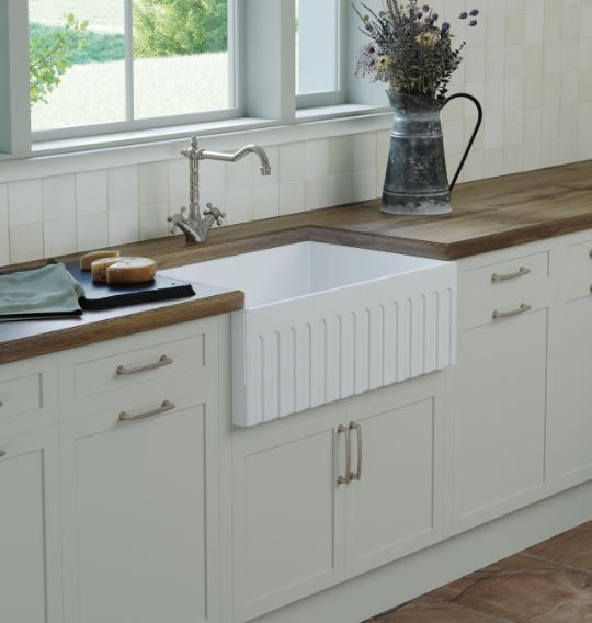 White kitchen sink beneath a window with wooden countertops and a vase of flowers