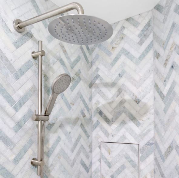 Modern shower with chrome showerhead and handheld sprayer against gray chevron tile.
