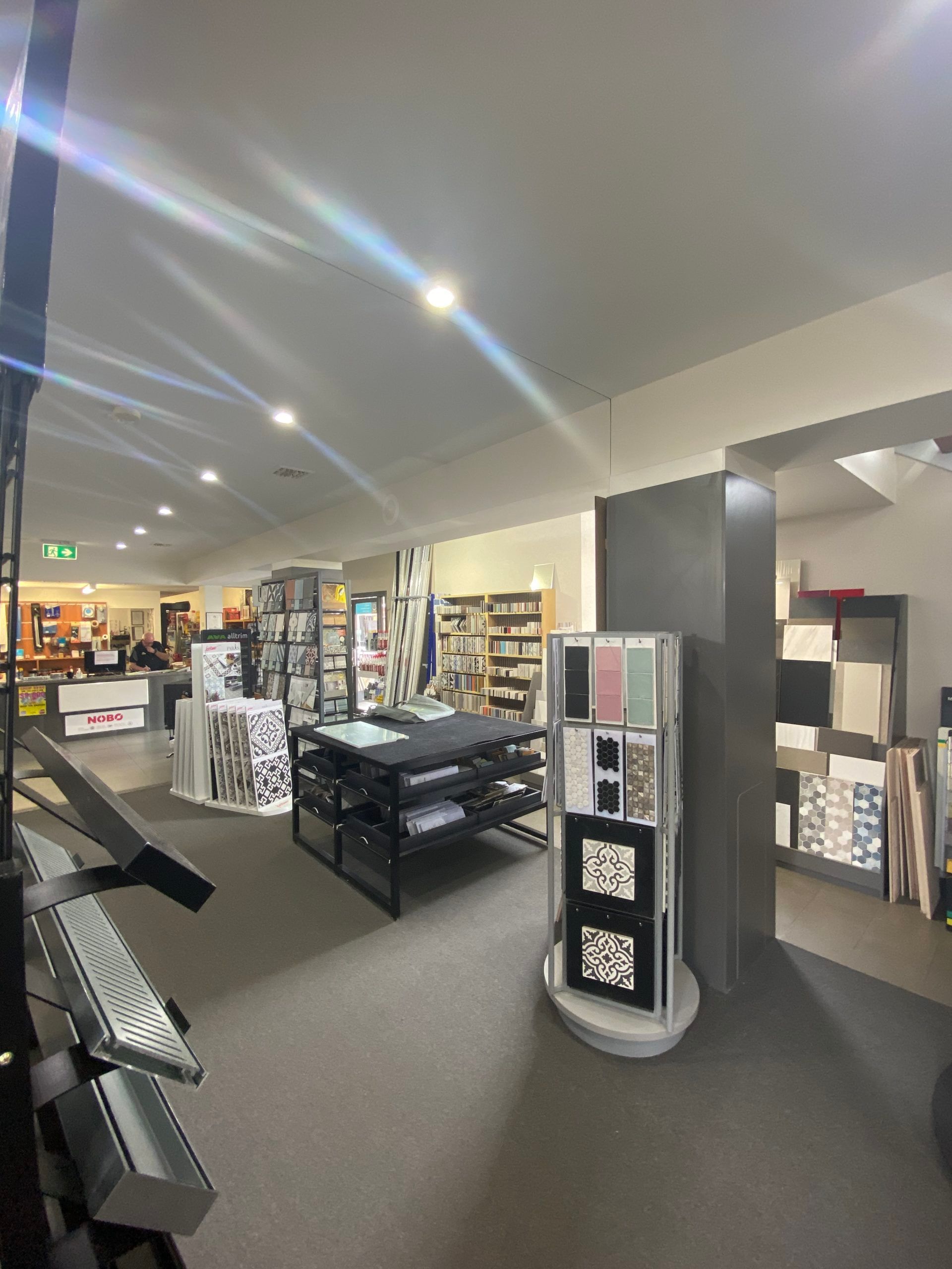Well-lit retail store aisle with shelves, display tables, and black carpet flooring