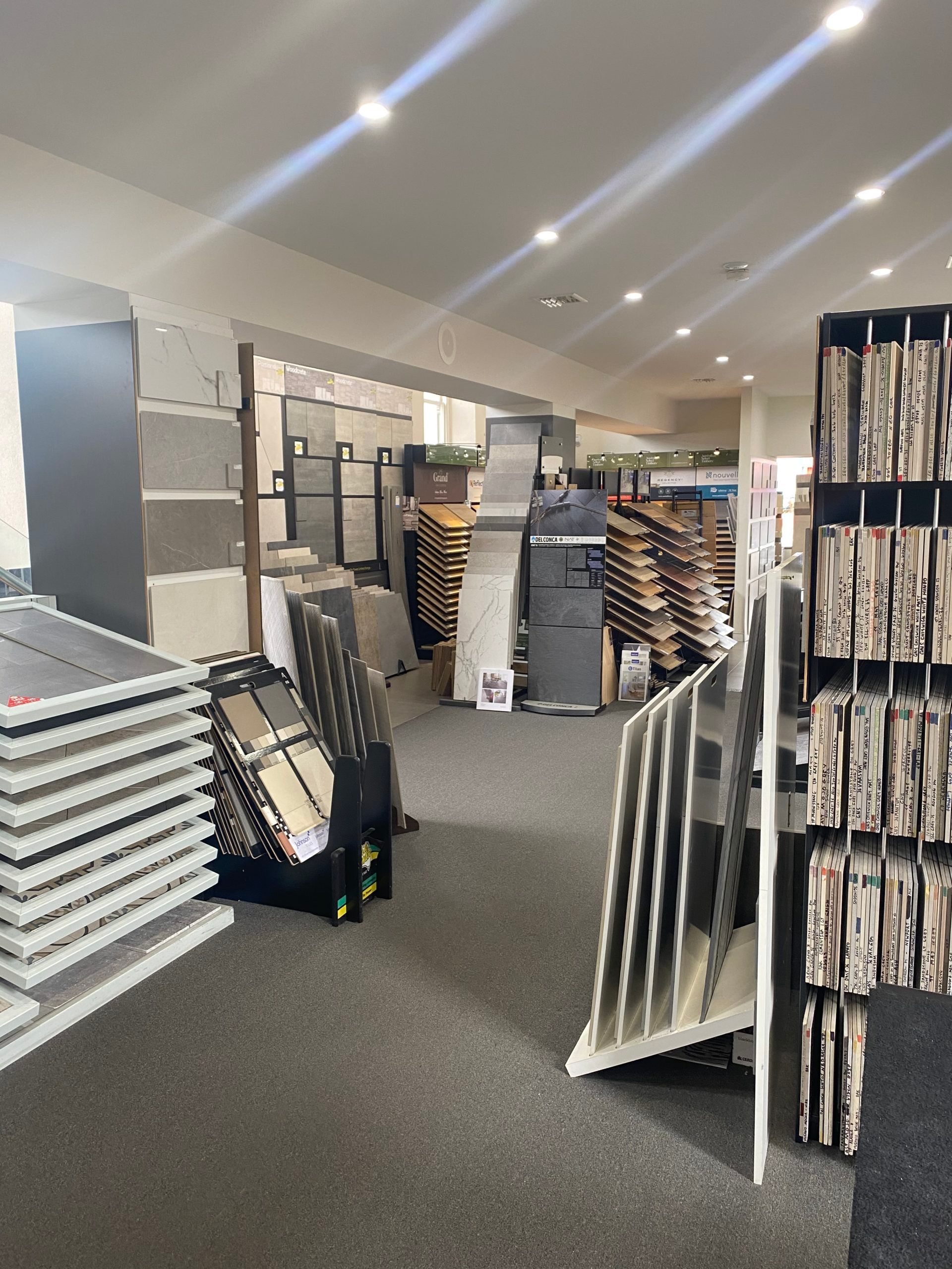 Carpet showroom aisle with stacked rugs and display samples under bright ceiling lights