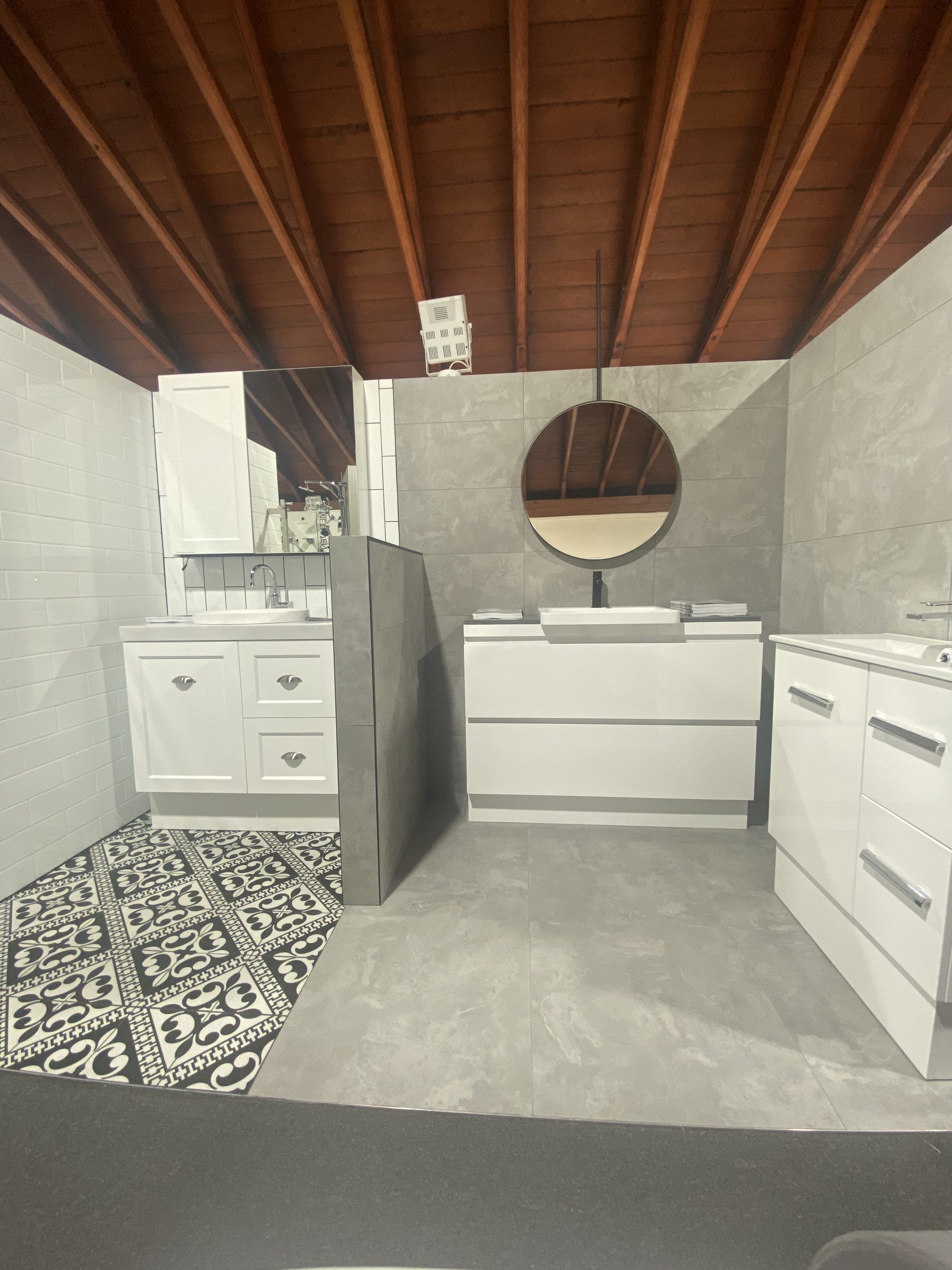 Bathroom with wooden ceiling, white vanity and sink, patterned floor mat, and round mirror.