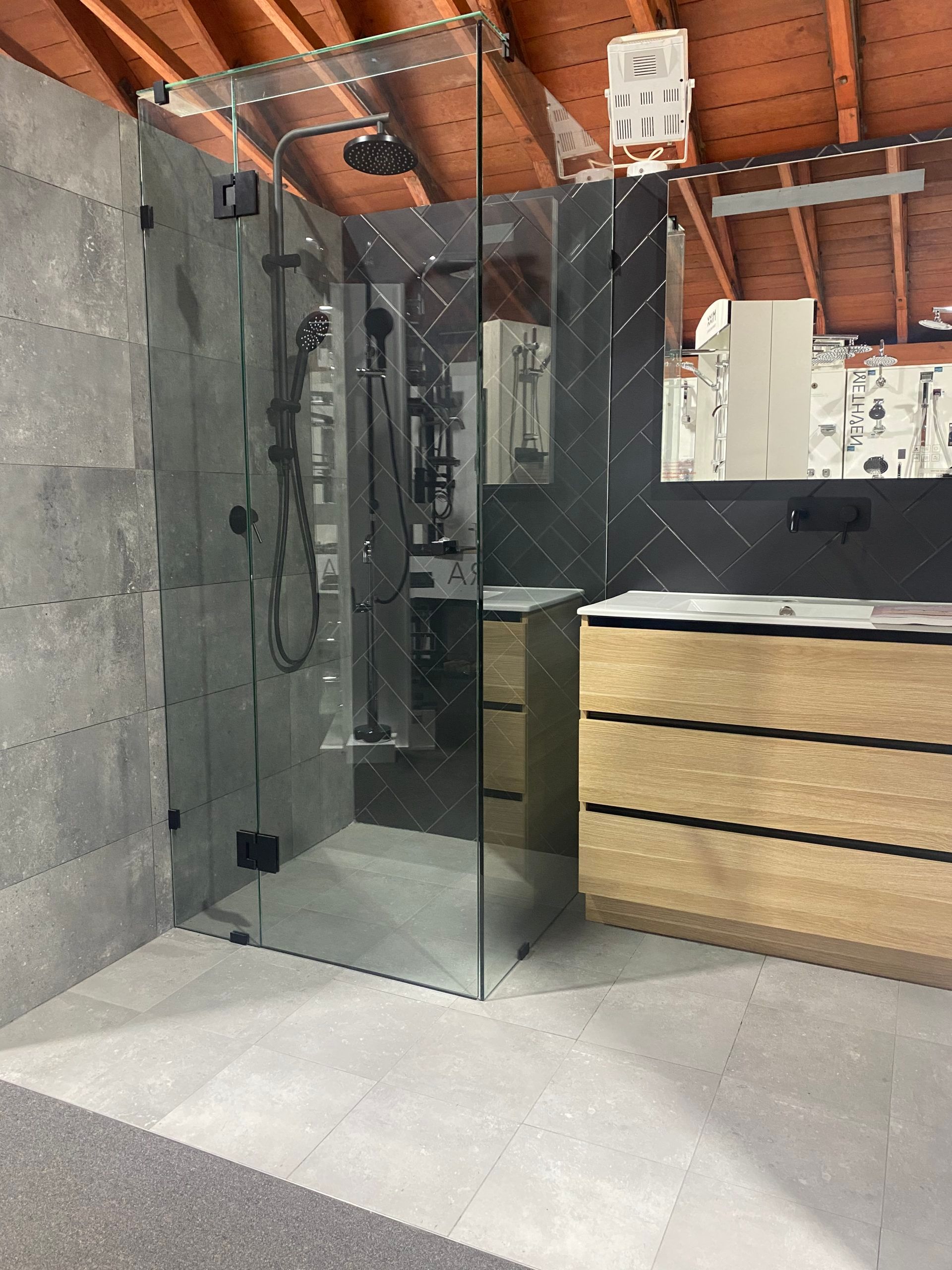 Glass shower enclosure in a modern bathroom with exposed wood ceiling and white tile floor