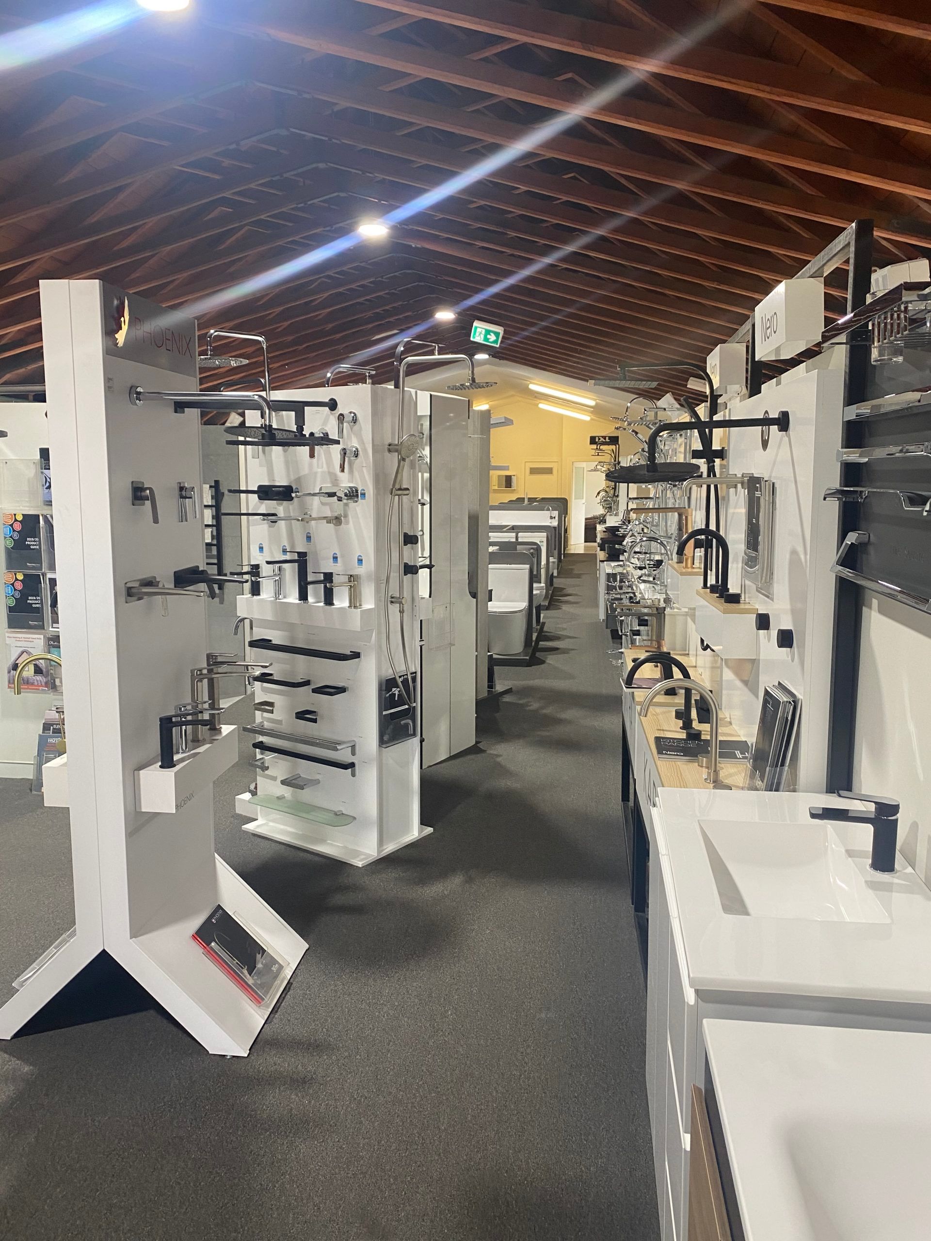 Indoor showroom aisle with white display racks and shelves under a wooden vaulted ceiling.