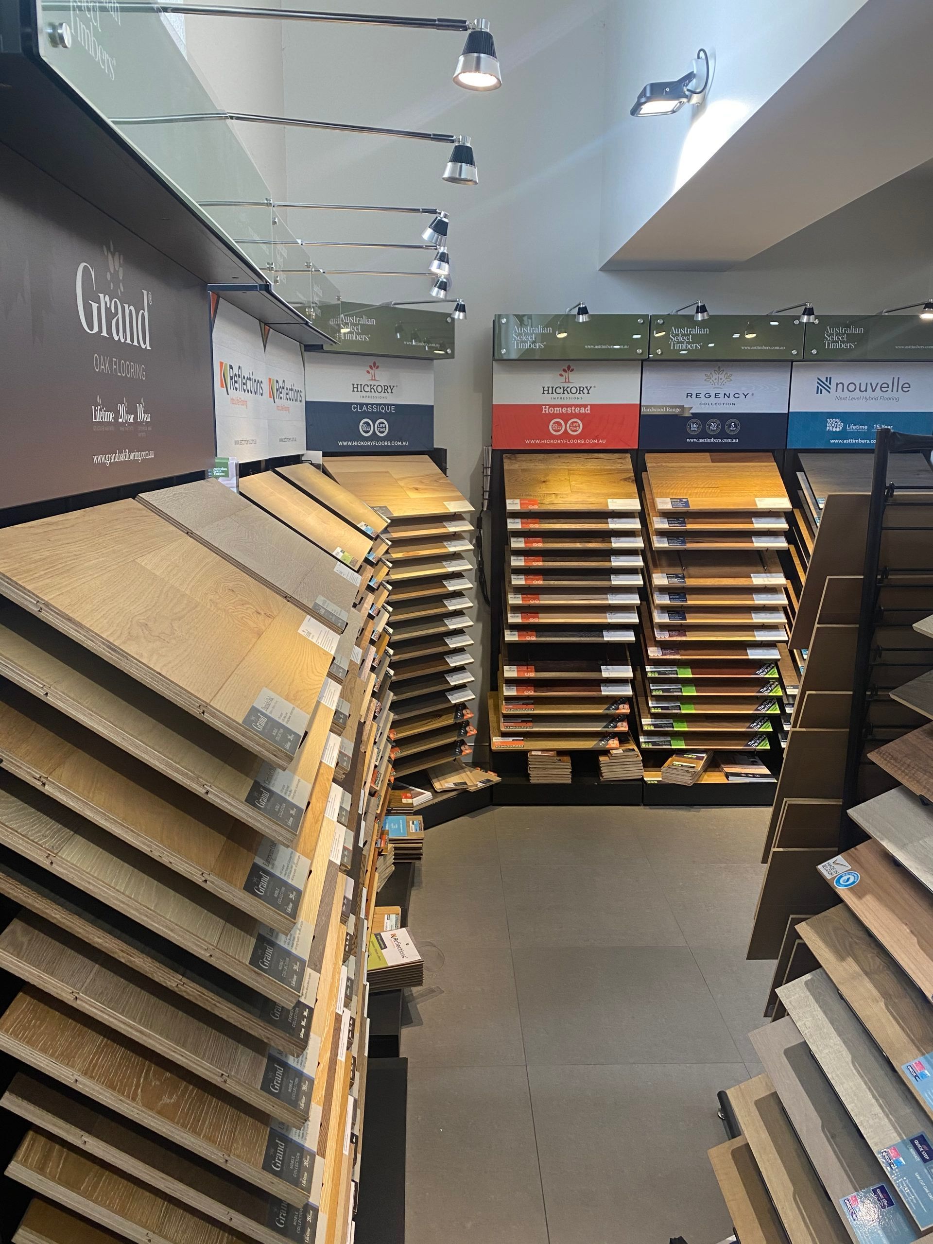 A flooring showroom aisle with rows of carpet and tile samples under bright ceiling lights.
