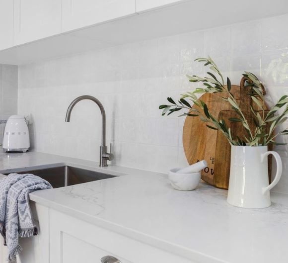 Minimal white kitchen counter with sink, faucet, toaster, and wooden cutting board with flowers