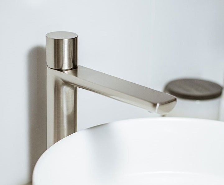 Modern chrome faucet beside a white sink, with a cylindrical handle and brushed metal finish