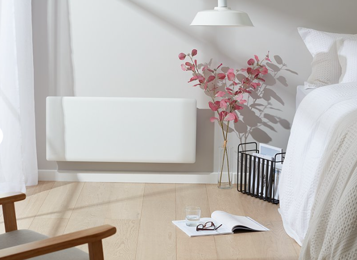 Minimal white bedroom with bed, radiator cover, pink flowers, and an open book on the floor