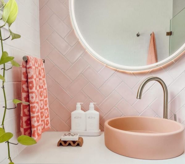 Pink bathroom sink with round mirror, white countertop, and coral towels on a pale pink wall