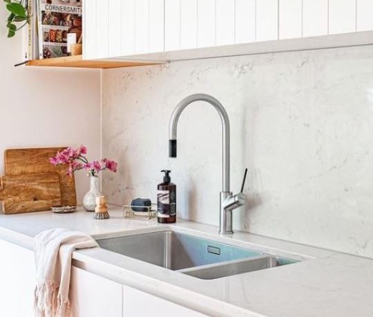Bright modern kitchen sink with silver faucet, white marble backsplash, and pink flowers on the counter
