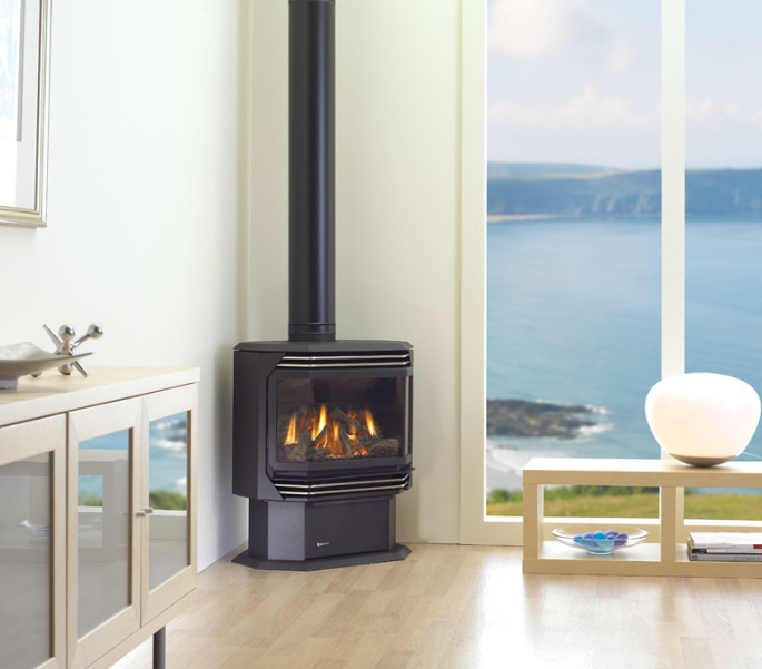 Modern living room with a black wood stove, light wood floors, and ocean views through large windows
