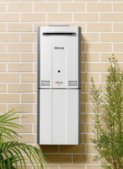 Wall-mounted white Rinnai unit on a tan brick wall, with plants in the foreground. Wall-mounted white Rinnai unit on a tan brick wall, with plants in the foreground.